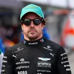 Fernando Alonso wearing Aston Martin F1 team clothing, a green cap and sunglasses in the paddock ahead of the 2026 Japanese Grand Prix.