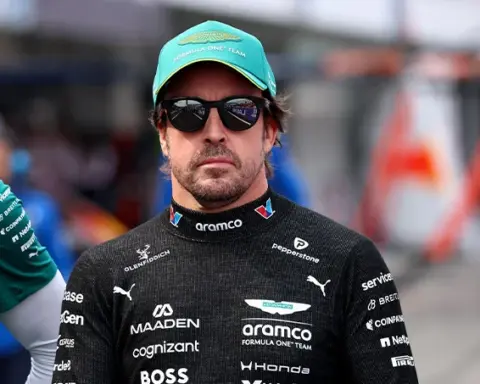 Fernando Alonso wearing Aston Martin F1 team clothing, a green cap and sunglasses in the paddock ahead of the 2026 Japanese Grand Prix.