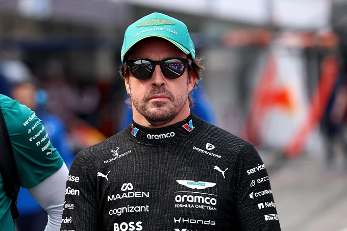 Fernando Alonso wearing Aston Martin F1 team clothing, a green cap and sunglasses in the paddock ahead of the 2026 Japanese Grand Prix.
