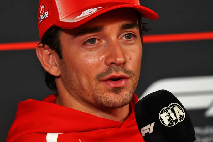 Charles Leclerc wearing a red Ferrari cap and team hoodie, speaking into an FIA Formula 1 microphone during Thursday's press conference at the 2026 Mexico City Grand Prix.