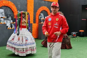 Charles Leclerc wearing Ferrari team clothing and a red cap beside a traditional Día de los Muertos display featuring a decorated skeleton and orange marigolds in Mexico City.