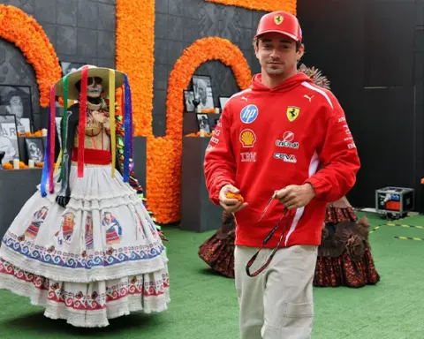 Charles Leclerc wearing Ferrari team clothing and a red cap beside a traditional Día de los Muertos display featuring a decorated skeleton and orange marigolds in Mexico City.